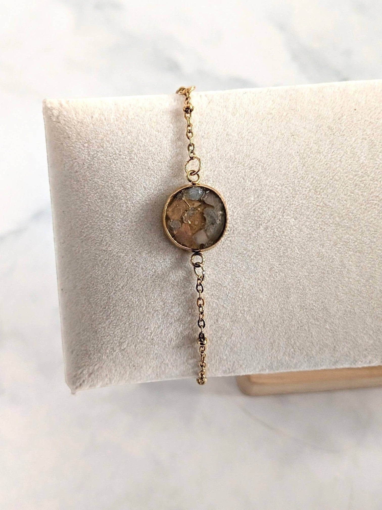 Nayuga Jewels armband med rosenkvarts och akvamarin i en rund 18k guldpläterad infattning på en vit smyckeskudde.