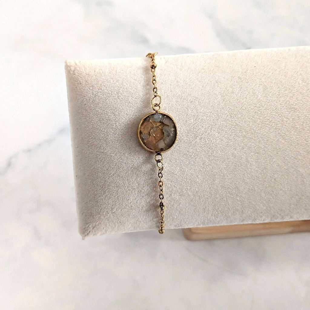 Nayuga Jewels armband med rosenkvarts och akvamarin i en rund 18k guldpläterad infattning på en vit smyckeskudde.