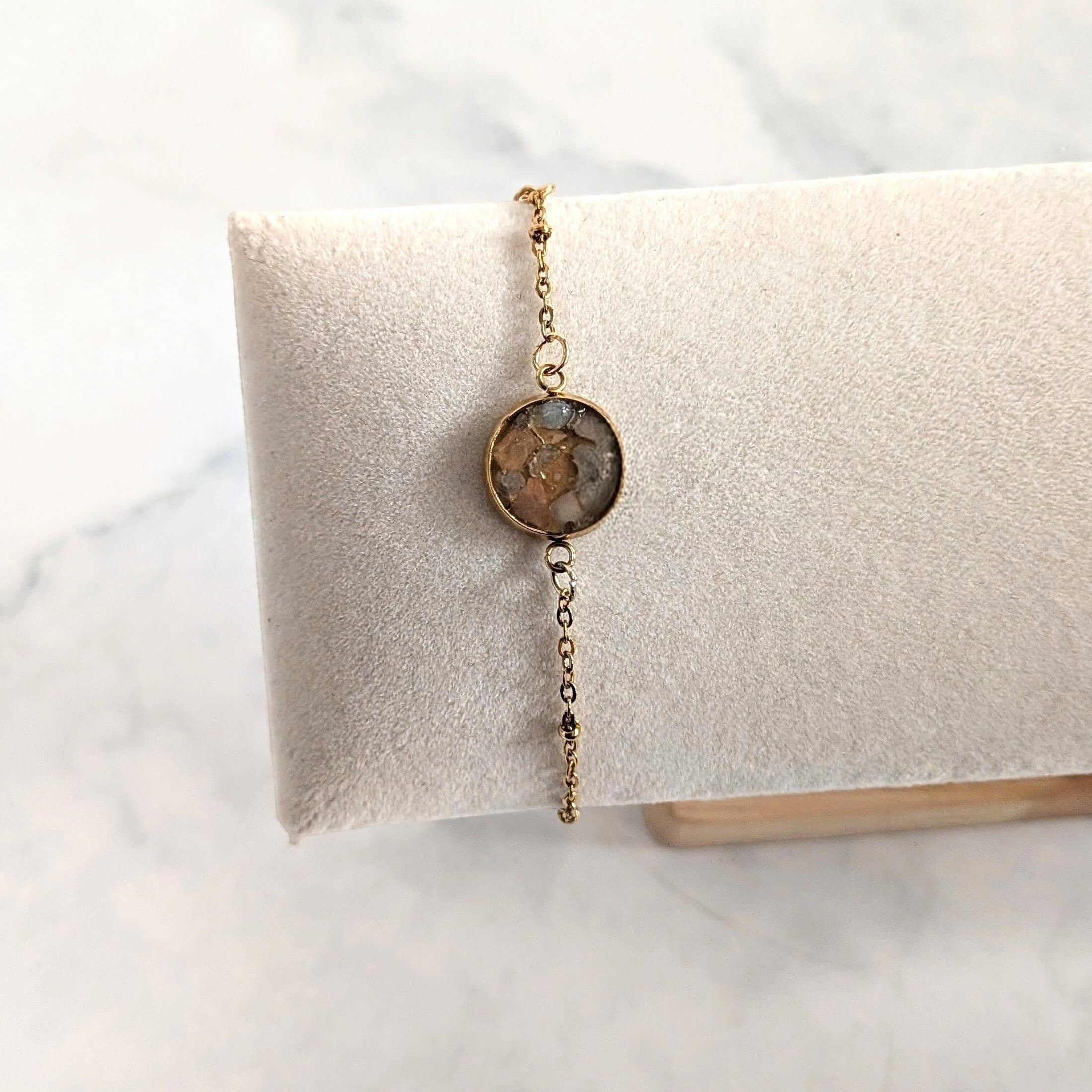 Nayuga Jewels armband med rosenkvarts och akvamarin i en rund 18k guldpläterad infattning på en vit smyckeskudde.
