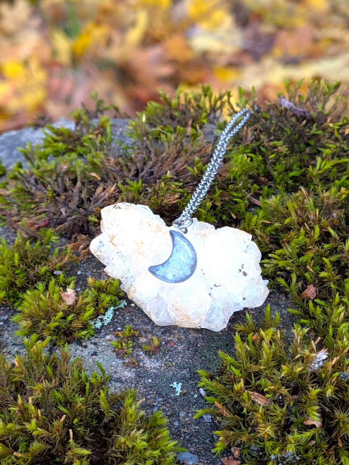 Citrinmagi halsband med halvmåne i silverpläterat stål och bergkristall, placerat på en rå bergkristall i mossa.