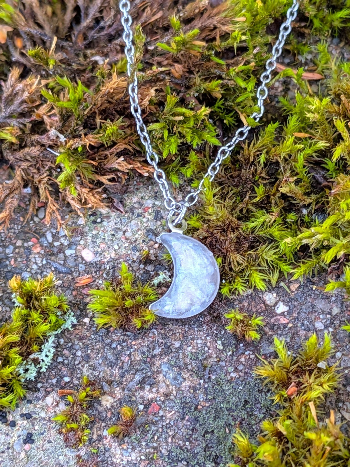 Citrinmagi halsband med halvmånehänge i silverpläterat stål och handinfattad bergkristall mot en bädd av mossa.