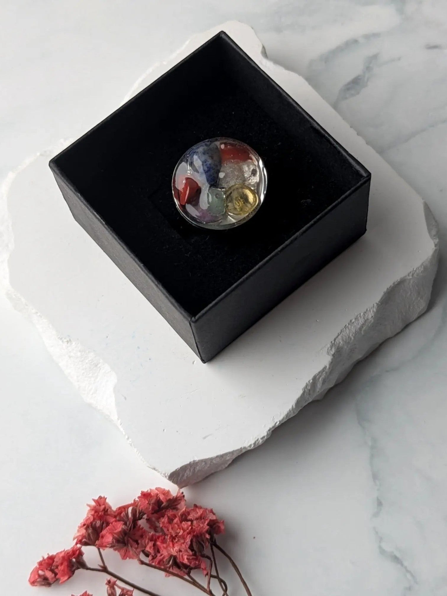 Citrinmagi handgjord chakra-ring i silverpläterat stål med sju olikfärgade kristaller i en svart ask.