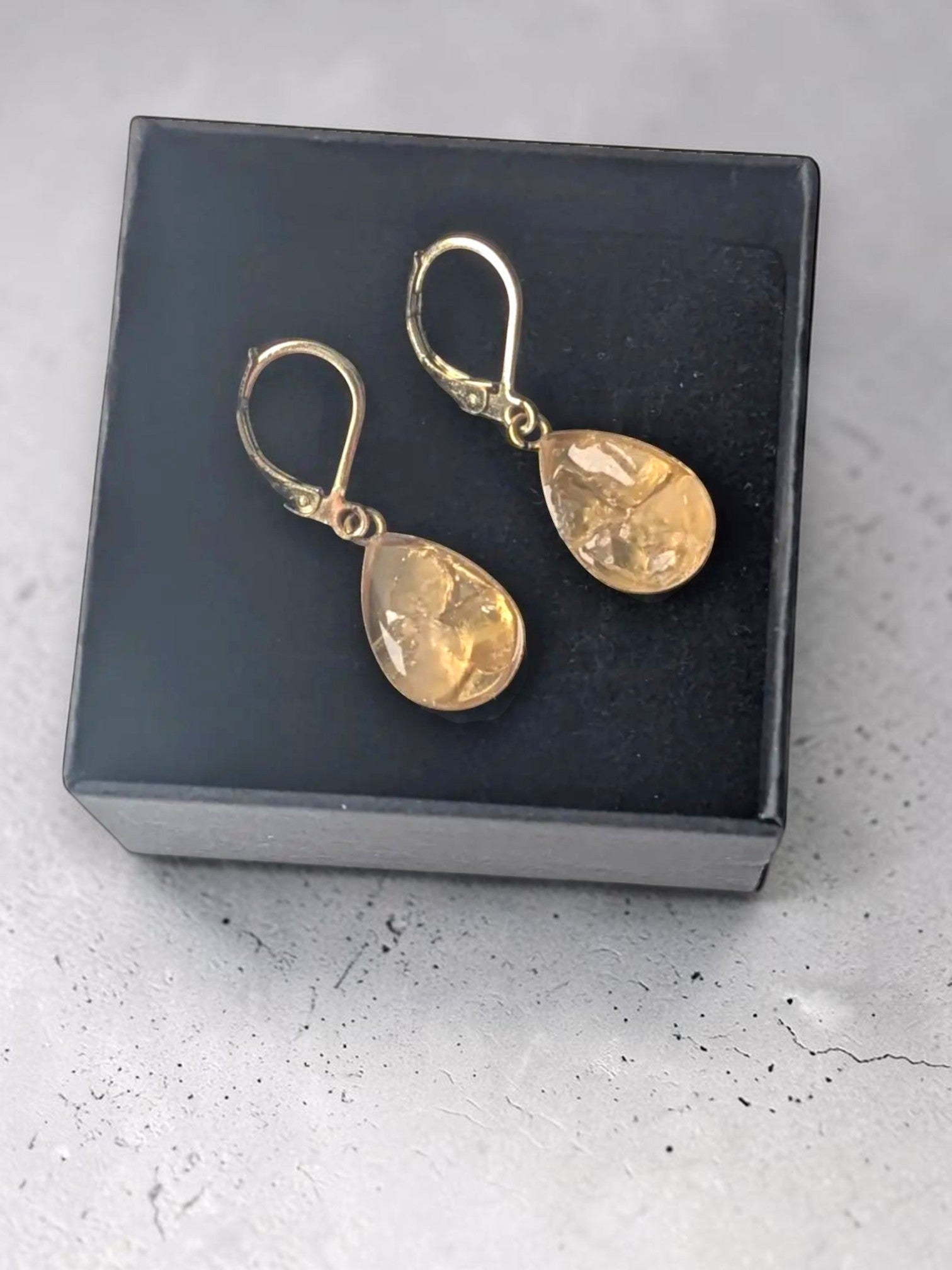 Citrinmagi örhängen med droppformade citrinkristaller i 18K guldpläterat stål, presenterade i en elegant ask.