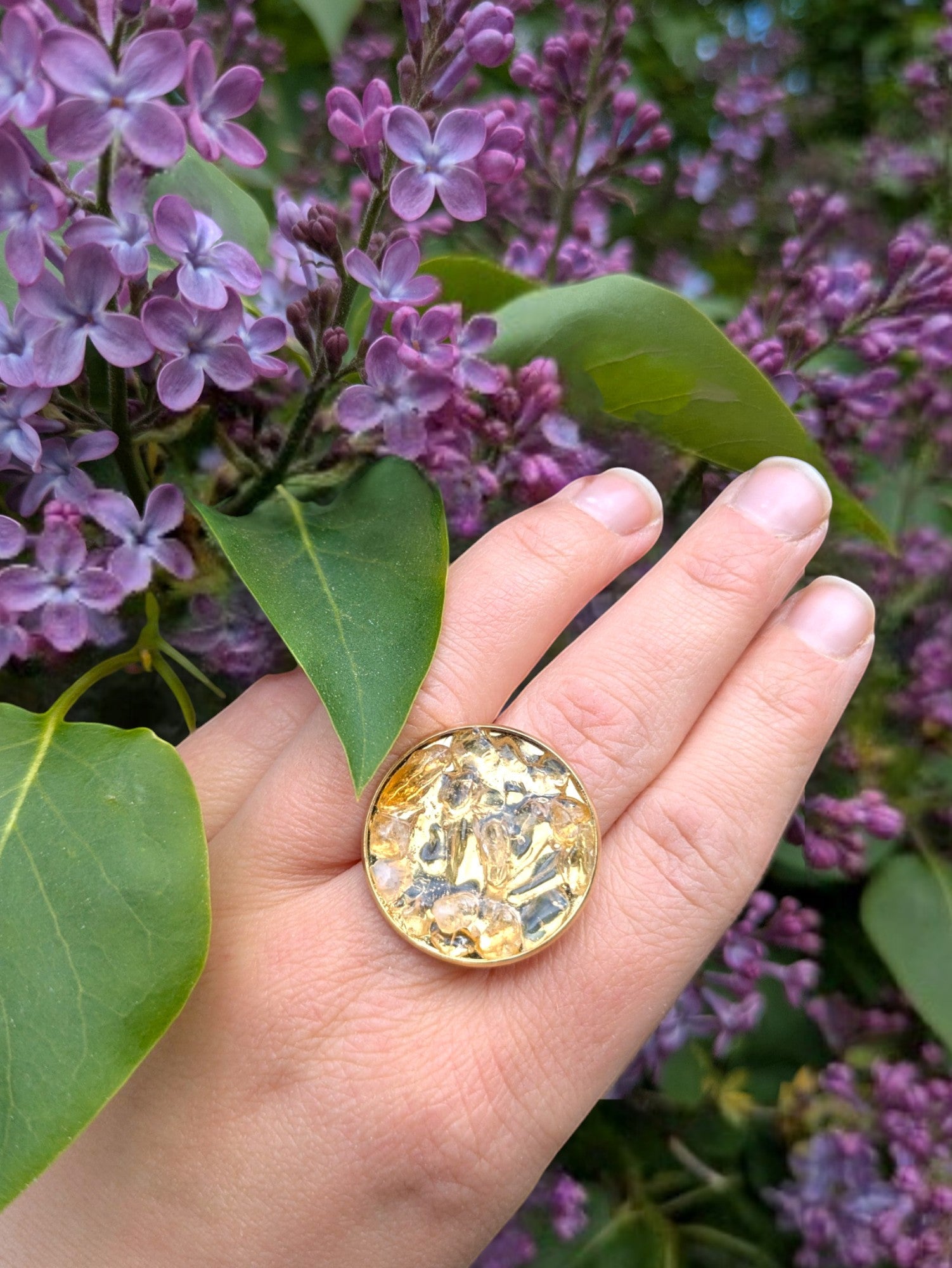 Citrinmagi justerbar ring i 18k guldpläterat stål med naturlig citrin, buren på hand framför blommande syrener.