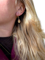 Citrinmagi droppformade örhängen i guld med glittrande sten som bärs av en kvinna med blont hår utomhus.