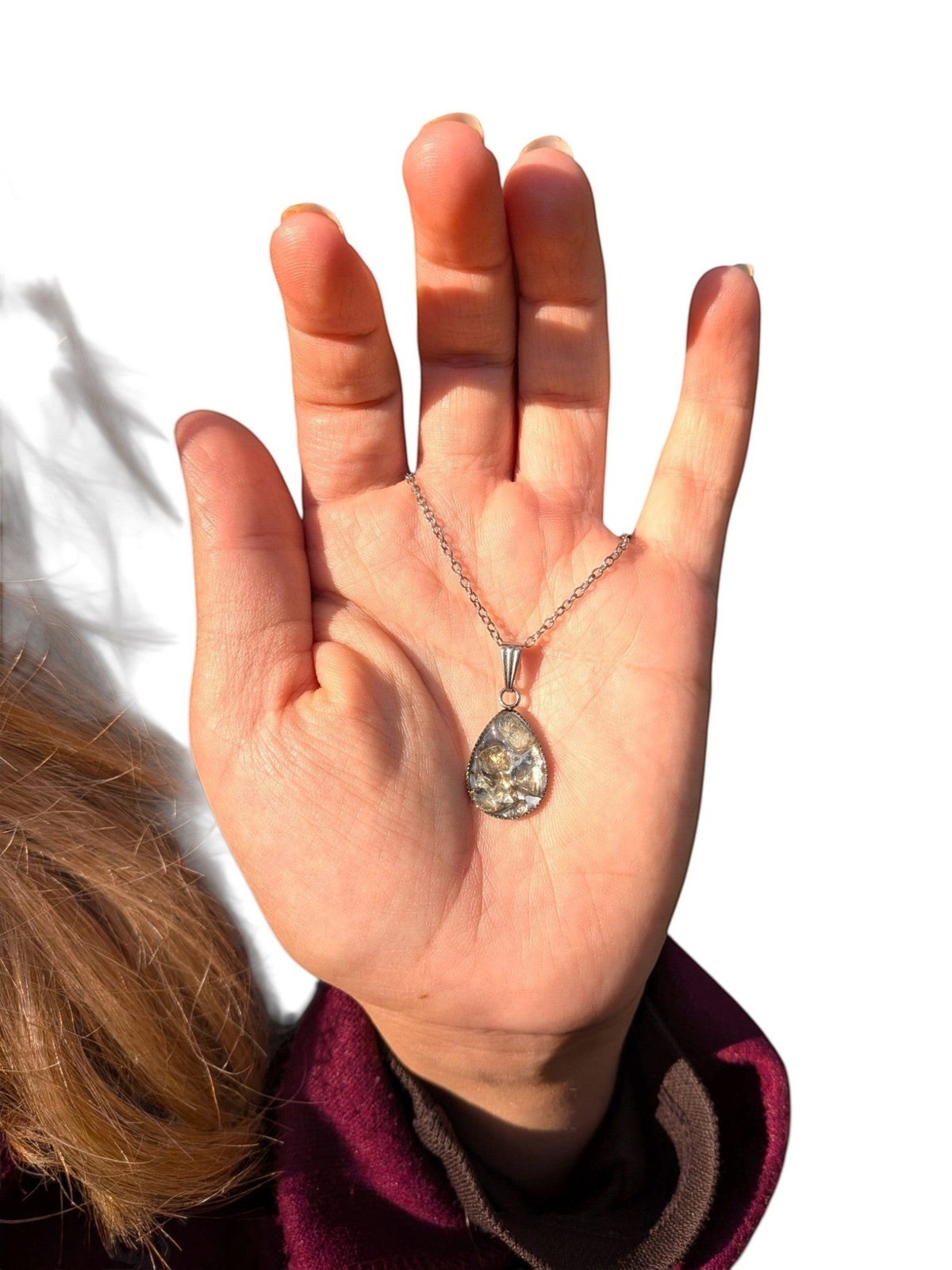 Citrinmagi droppformat halsband med texturerad sten i silverfärgad infattning som hålls i en hand utomhus.