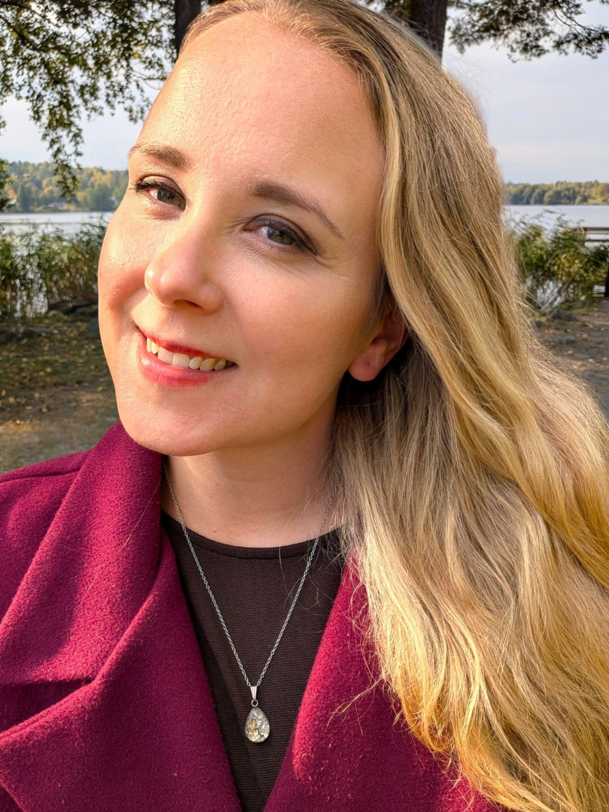 Kvinna bär ett elegant droppformat halsband från Citrinmagi med en texturerad sten i en vacker utomhusmiljö vid sjön.