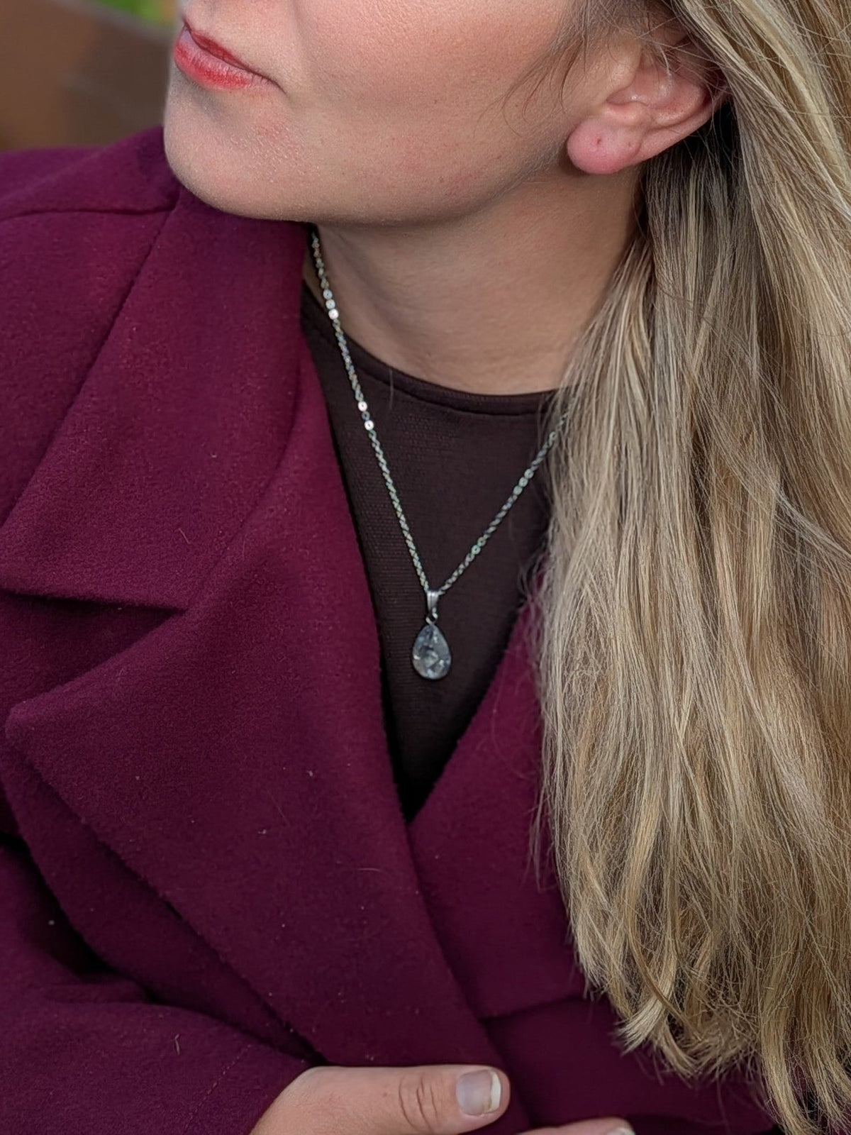 Citrinmagi droppformat halsband med texturerad sten på silverkedja buret av kvinna i vinröd kappa utomhus