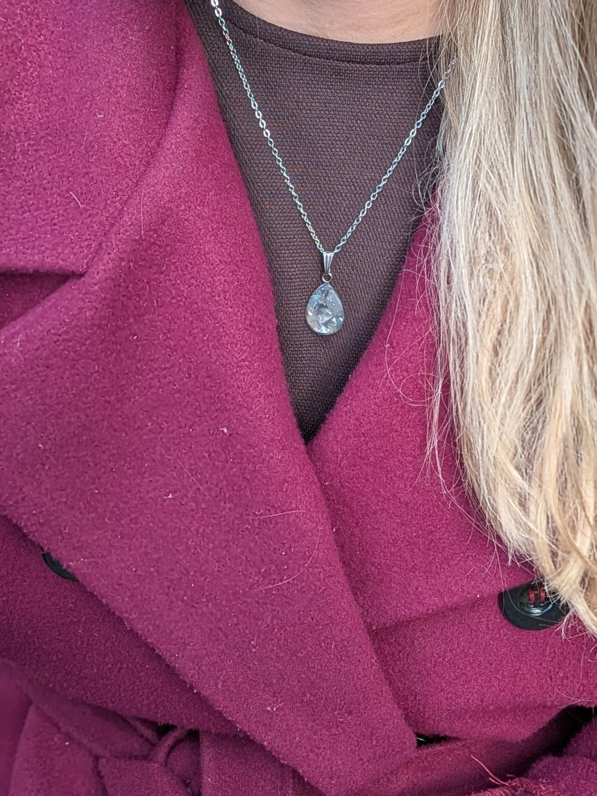 Citrinmagi droppformat halsband med sten i silverfärgad kedja buret av kvinna i vinröd kappa