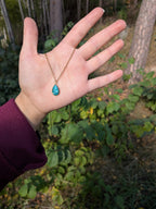 Citrinmagi halsband med droppformat turkost hänge i guldfärgad infattning och tunn kedja, hållet i en hand utomhus.