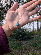 Citrinmagi droppformat halsband med turkos sten och guldfärgad kedja som hålls i en hand utomhus.