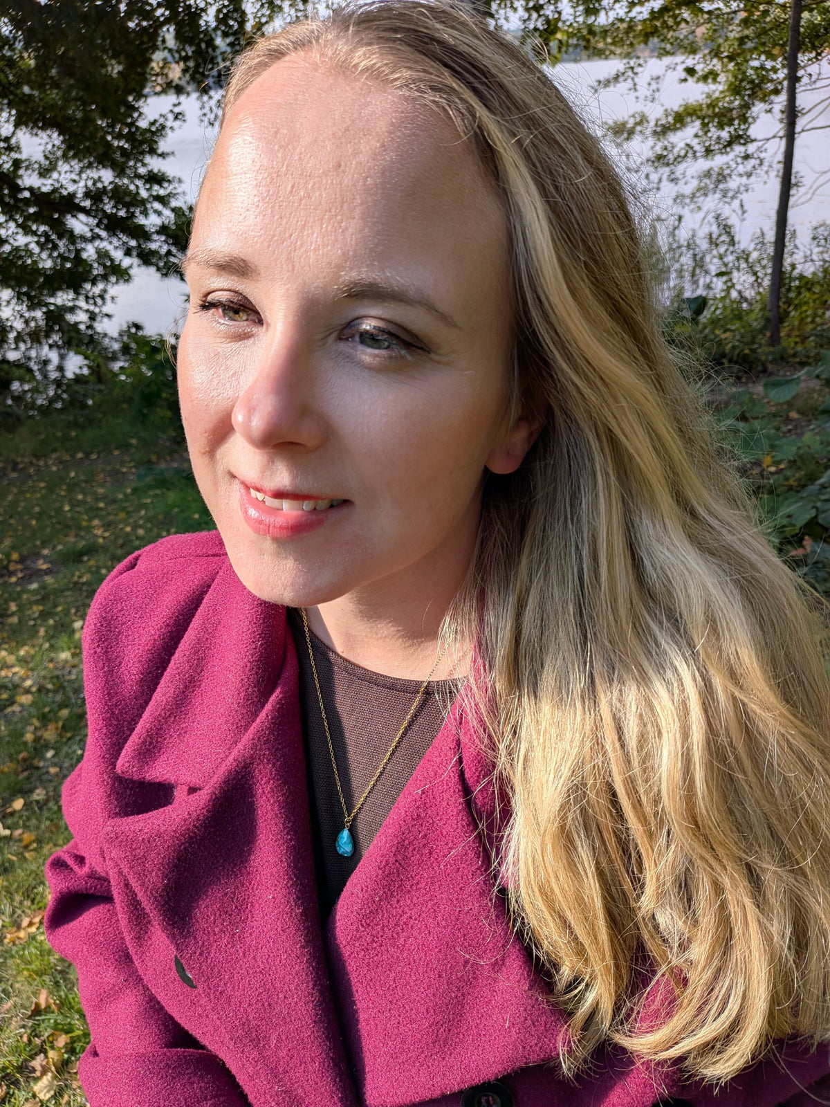 Citrinmagi halsband med droppformat turkost hänge i guldfärgad infattning buret av kvinna i vinröd kappa utomhus