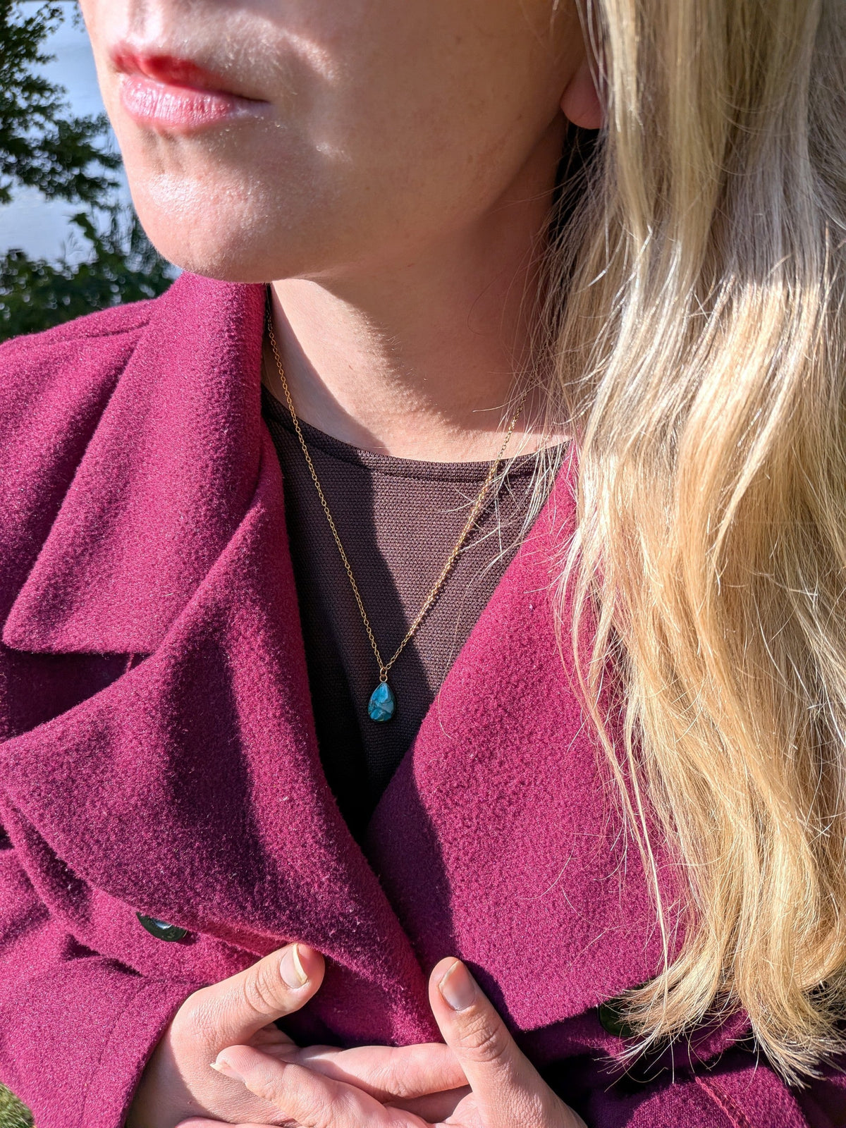 Citrinmagi halsband med droppformat turkost hänge i guldfärgad infattning och tunn guldkedja buret av en kvinna.