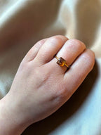 Citrinmagi ring med fyrkantig karneolsten i 18k guldpläterat stål buren på ett finger mot ett sidenliknande tyg