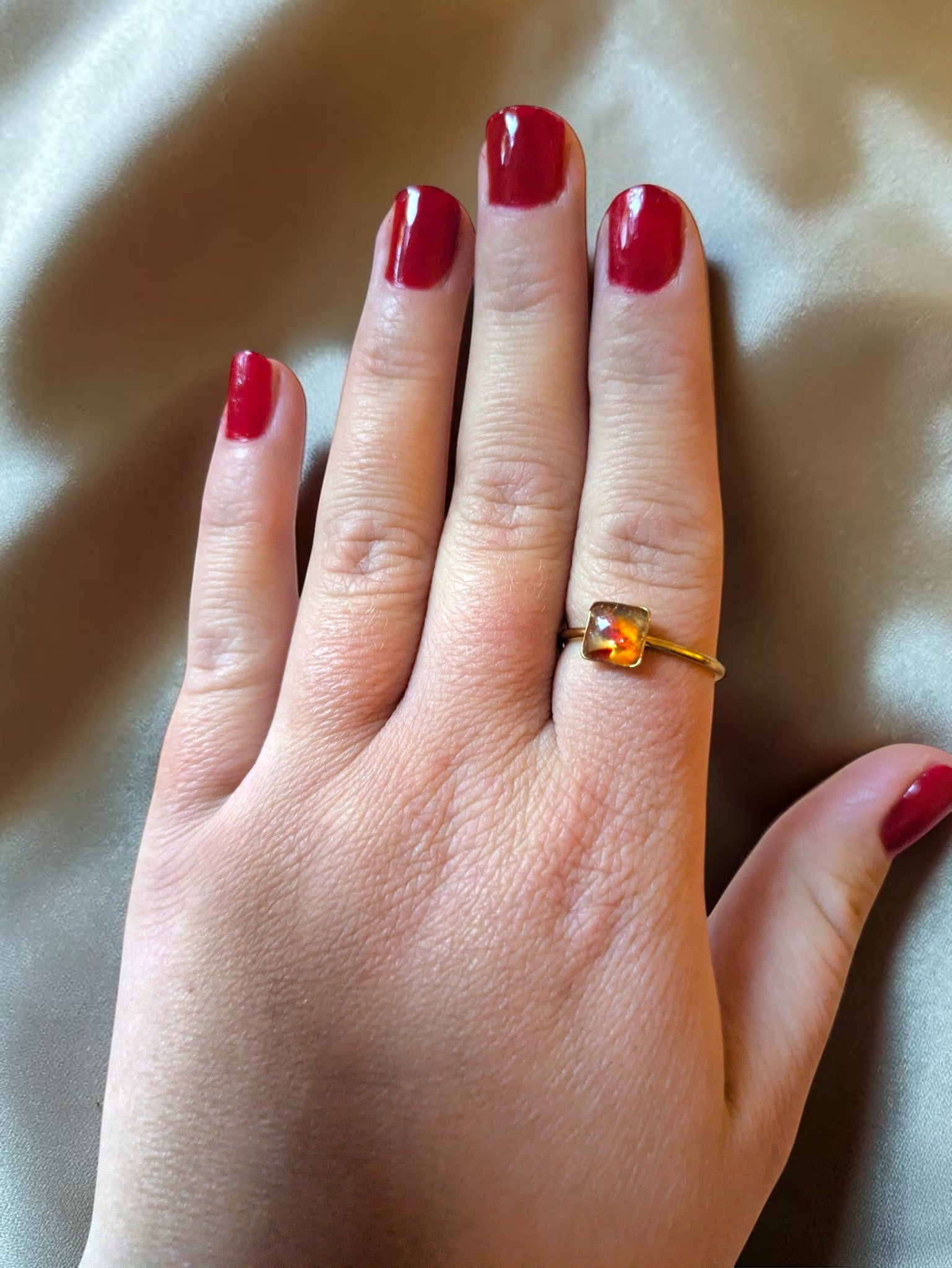 Citrinmagi fyrkantig guldring med naturlig karneolkristall buren på ett finger mot en sidenbakgrund.