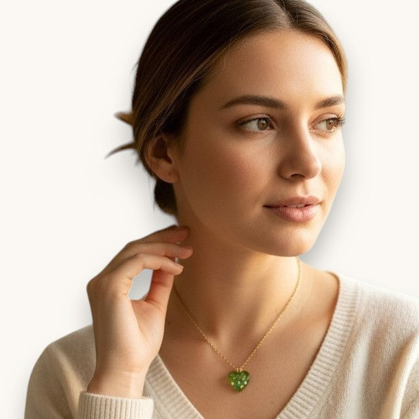Kvinna bär Citrinmagi halsband med hjärtformad grön aventurin i 18K guldpläterat stål vid ett fönster.