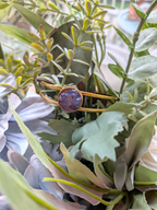Citrinmagi guldtonat armband med öppen design och en rund lila dekorativ detalj placerat bland gröna blad.