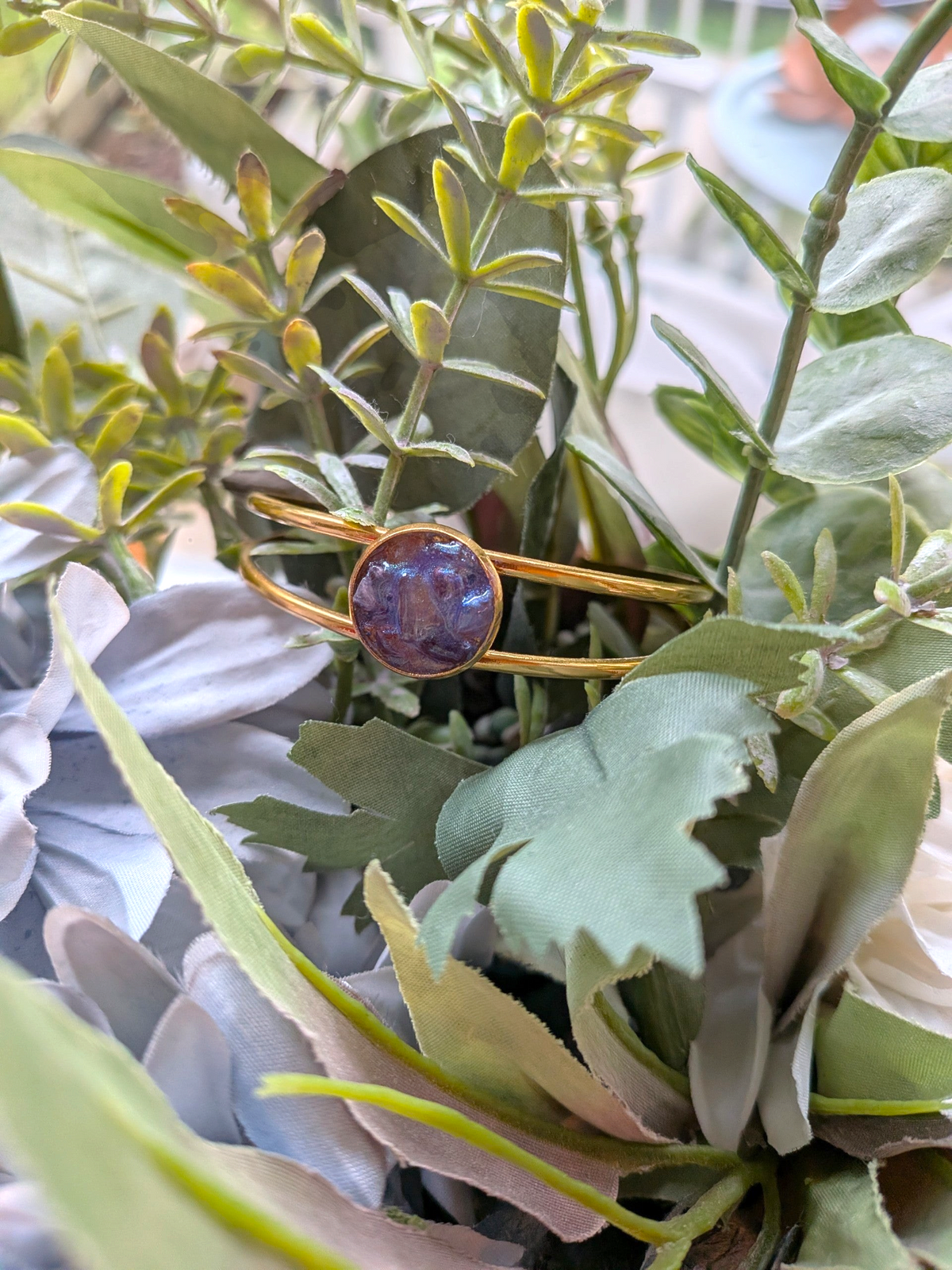 Citrinmagi guldtonat armband med öppen design och en rund lila dekorativ detalj placerat bland gröna blad.
