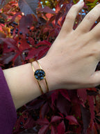 Citrinmagi guldtonat cuff-armband med mörkblå gnistrande stenar på en handled mot en bakgrund av röda höstlöv.