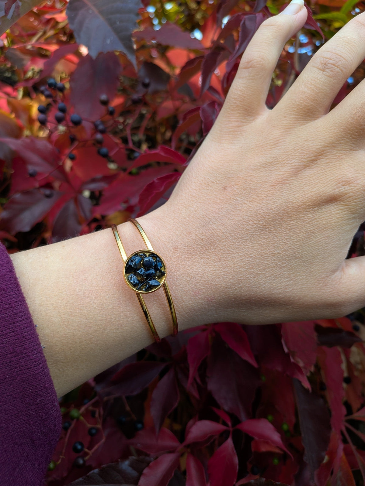 Citrinmagi guldtonat cuff-armband med mörkblå gnistrande stenar på en handled mot en bakgrund av röda höstlöv.