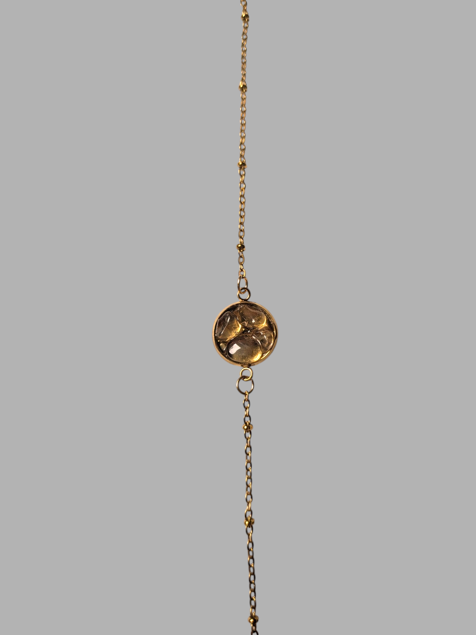 Citrinmagi armband i guld med fin kedja, små kuldetaljer och en rund bärnstensliknande sten i mitten.