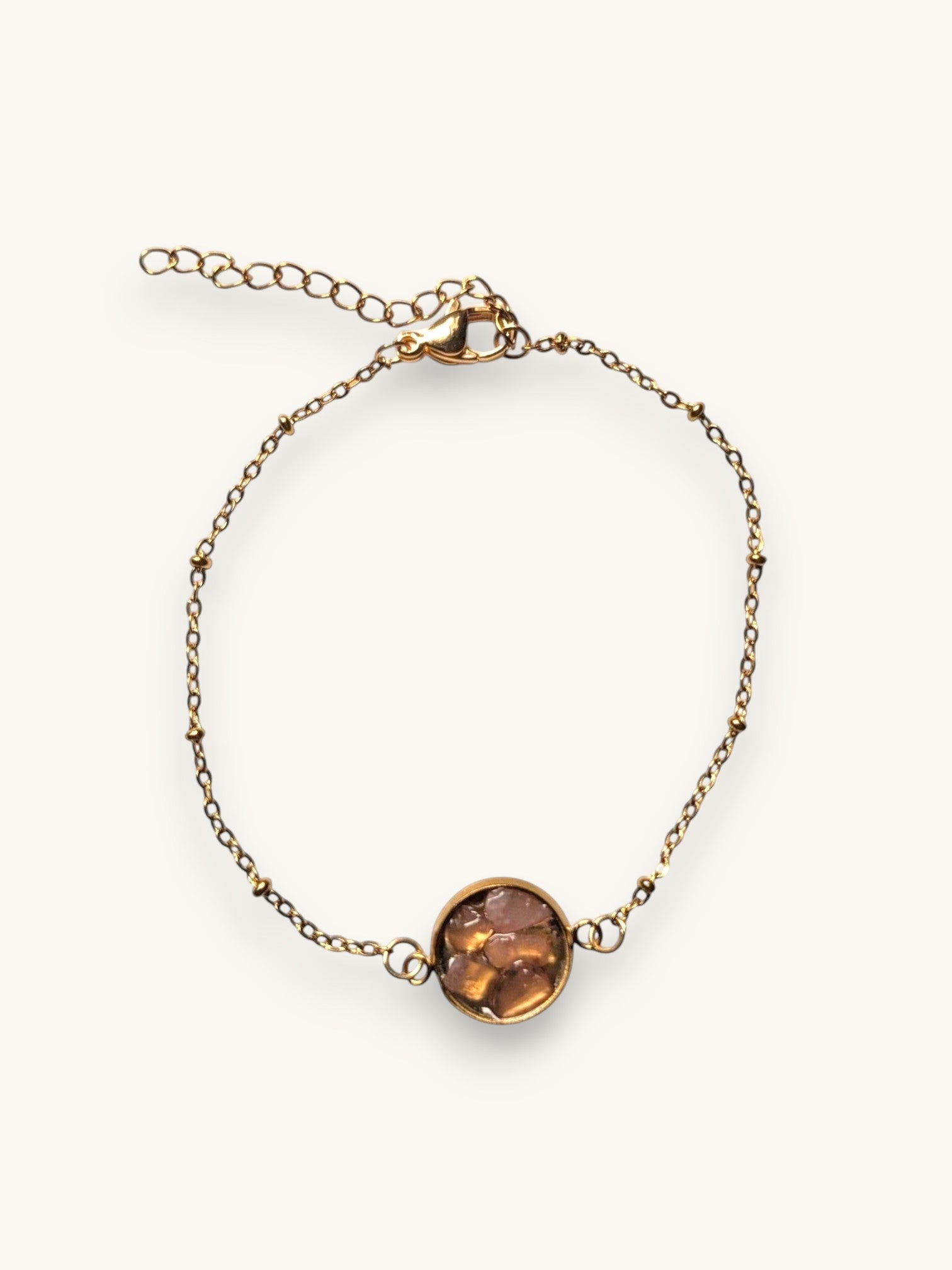 Citrinmagi armband i guldtonad metall med en rund detalj fylld av slipade stenar i varma jordnära nyanser.