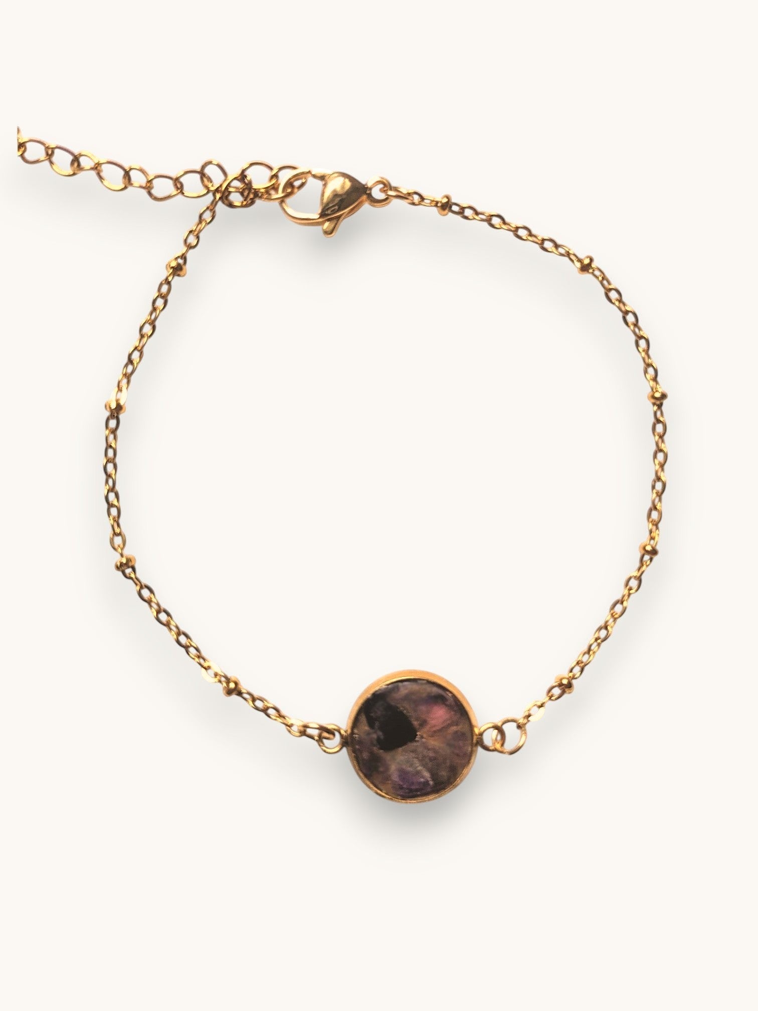 Citrinmagi armband med guldfärgad kedja och rund infattning med lila och svarta ädelstenar på vit marmoryta