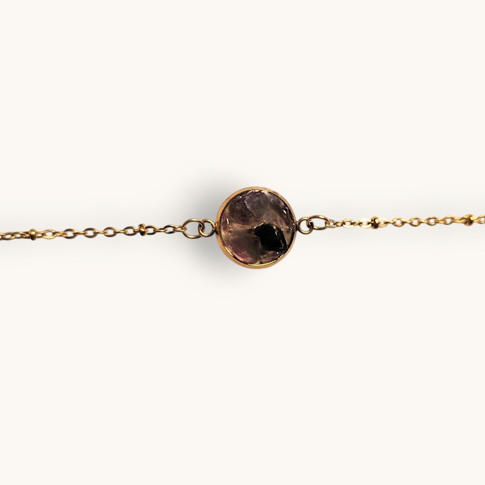 Citrinmagi armband med guldfärgad kedja och rund infattning med lila och svarta ädelstenar på vit marmoryta