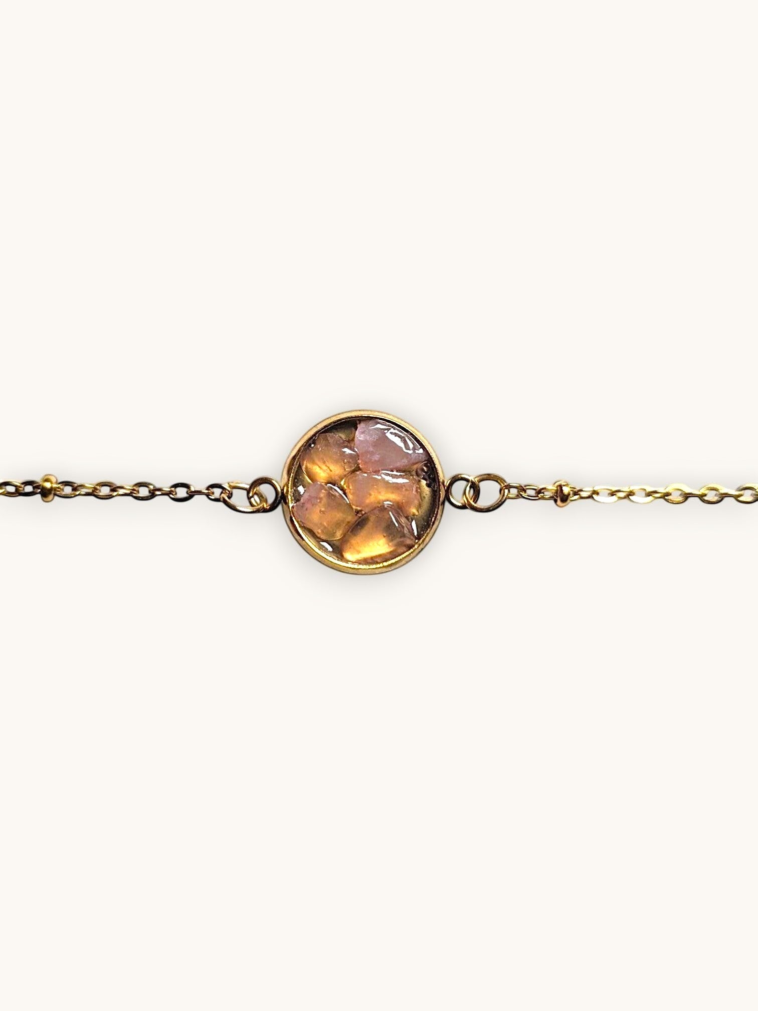 Citrinmagi guldtonat armband med rund detalj fylld av slipade stenar i varma jordnära nyanser på marmorbakgrund