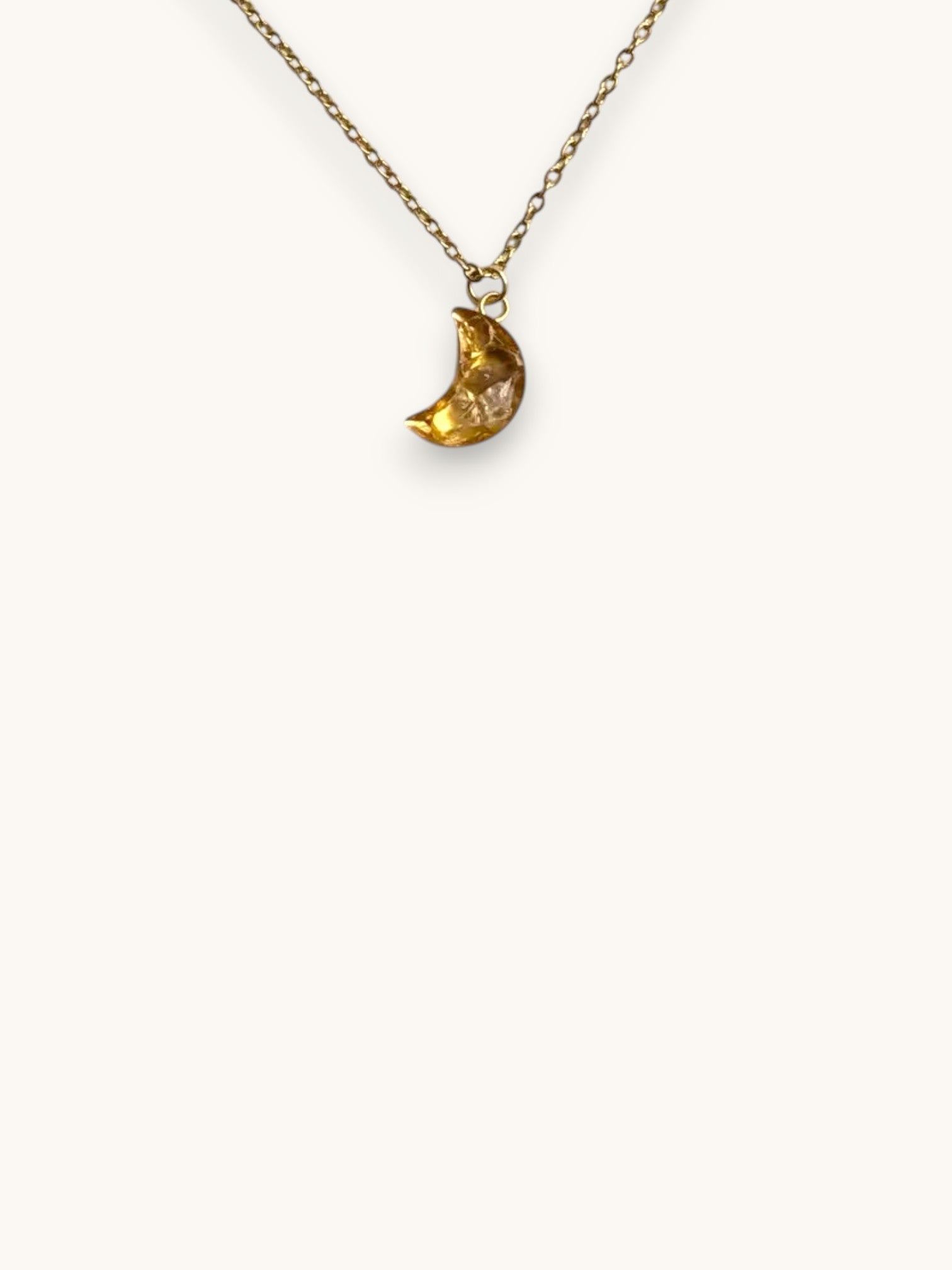 Citrinmagi halsband med en guldfärgad måne och äkta citrin på en vit stenplatta med en liten torkad blomma.