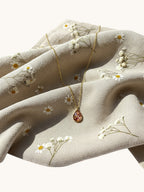 Citrinmagi halsband med droppformad granat i 18k guldpläterat stål, placerat på ett blommigt tyg.