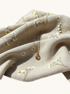 Citrinmagi halsband med droppformad granat i guldpläterad infattning på ett beige tyg med blommönster.