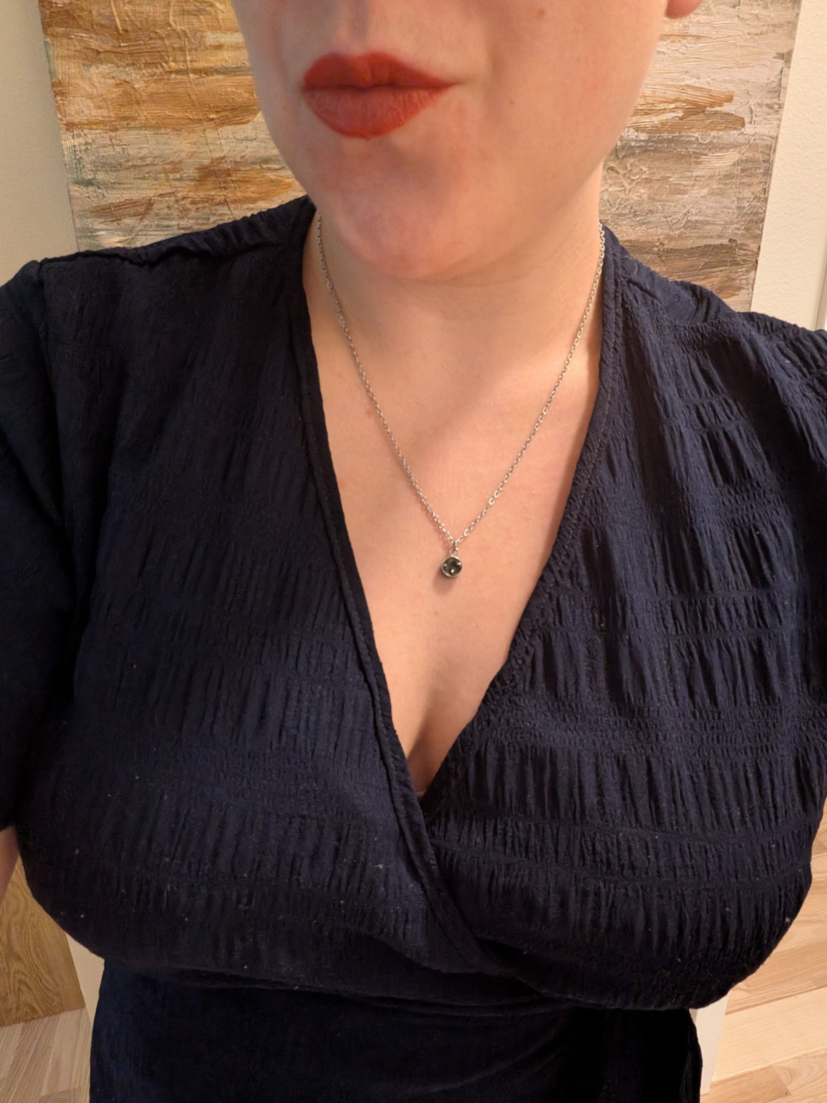 Citrinmagi halsband med rund svart onyxsten i silverpläterat stål buret av en kvinna i mörkblå klänning.