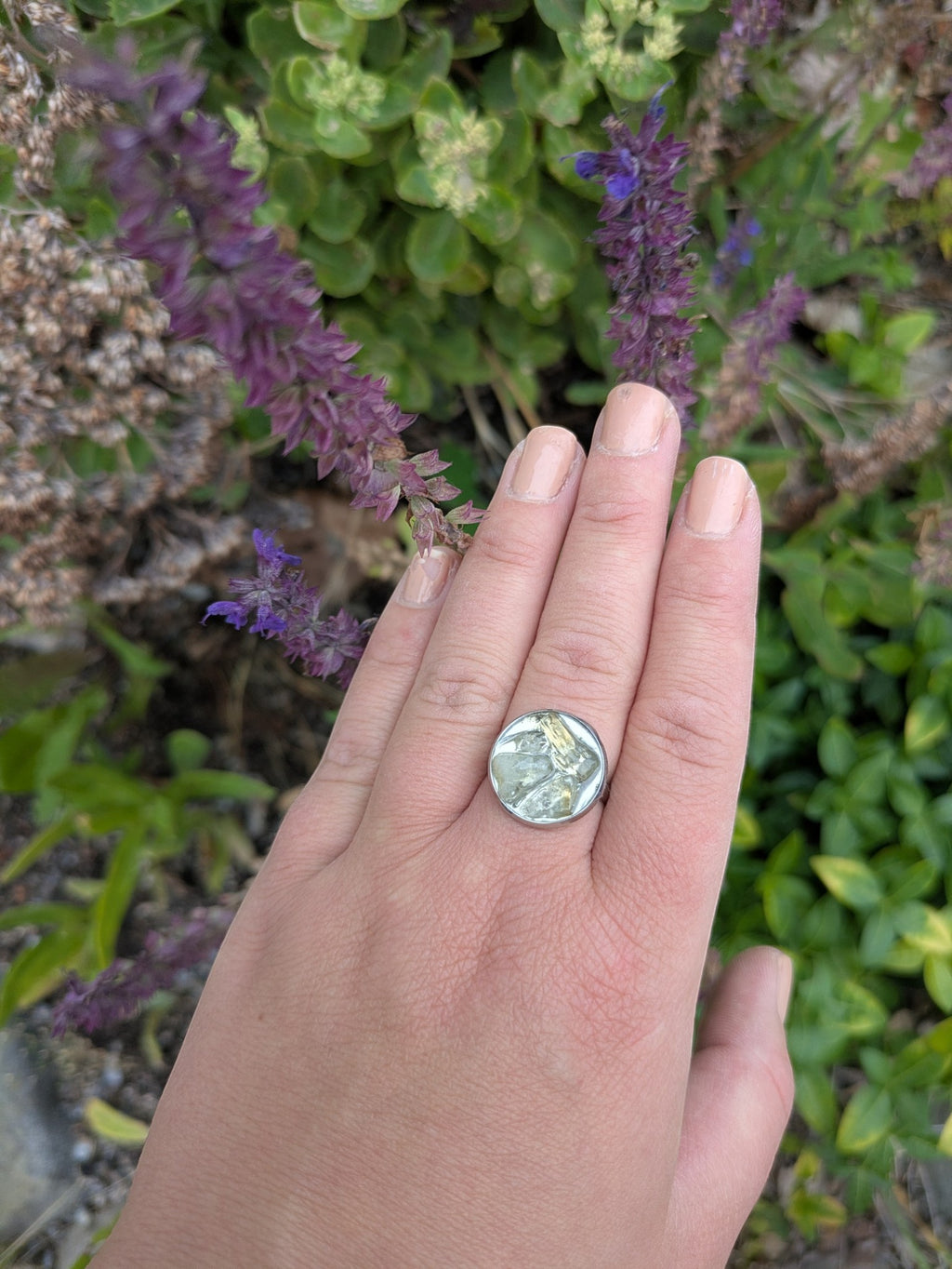 Citrinmagi handgjord ring i silverfärgad metall med en unik texturerad grön sten, buren på en hand utomhus.