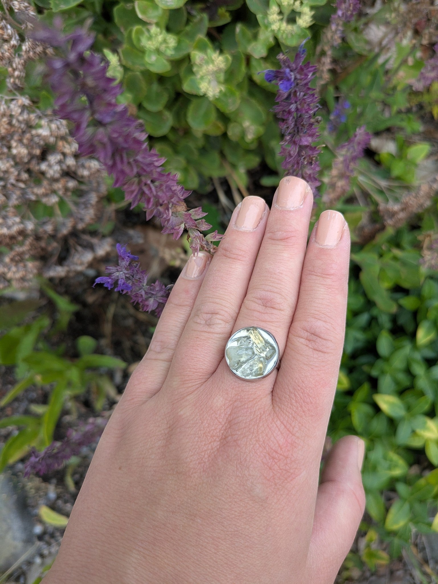 Citrinmagi handgjord ring i silverfärgad metall med en unik texturerad grön sten, buren på en hand utomhus.