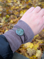 Citrinmagi handgjort cuff-armband i mörk metall med gröna slipade stenar buret på en handled med stickad tröja.