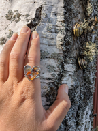 Citrinmagi hjärtformad ring i silverfärgad metall med mosaik av bärnstensfärgade stenar på en björkstam