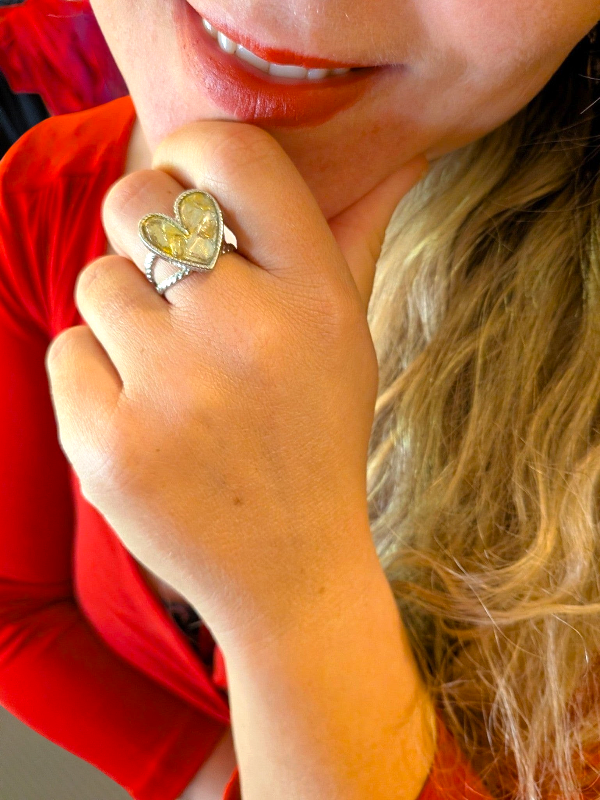 Citrinmagi hjärtformad ring i silverfärgad metall med tvinnad skena buren på ett finger av en kvinna i röd tröja