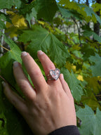 Citrinmagi hjärtformad ring i sterling silver med tvinnad skena och texturerad yta, buren på ett finger mot lönnlöv.