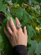 Citrinmagi hjärtformad ring i sterling silver med tvinnad skena och texturerad yta, buren på en hand mot gröna blad.