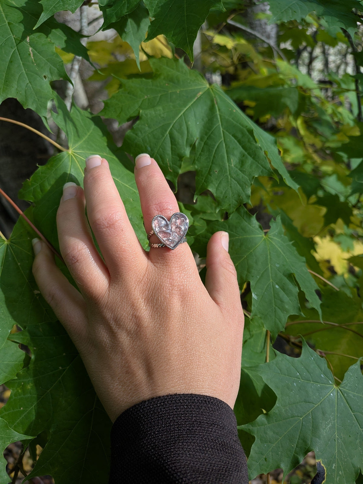 Citrinmagi hjärtformad ring i sterling silver med tvinnad skena och texturerad yta, buren på en hand mot gröna blad.