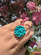 Citrinmagi ring i guld med turkosa howlit-kristaller, hållen mot en bakgrund av blommande rosa grenar.