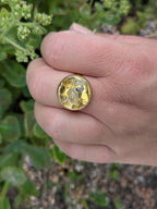 Citrinmagi justerbar ring i 18k guldpläterat stål med en rund, naturlig citrinkristall på ett finger utomhus.