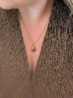 Citrinmagi halsband med droppformad karneol i guldpläterad ram buret av kvinna i glittrig topp