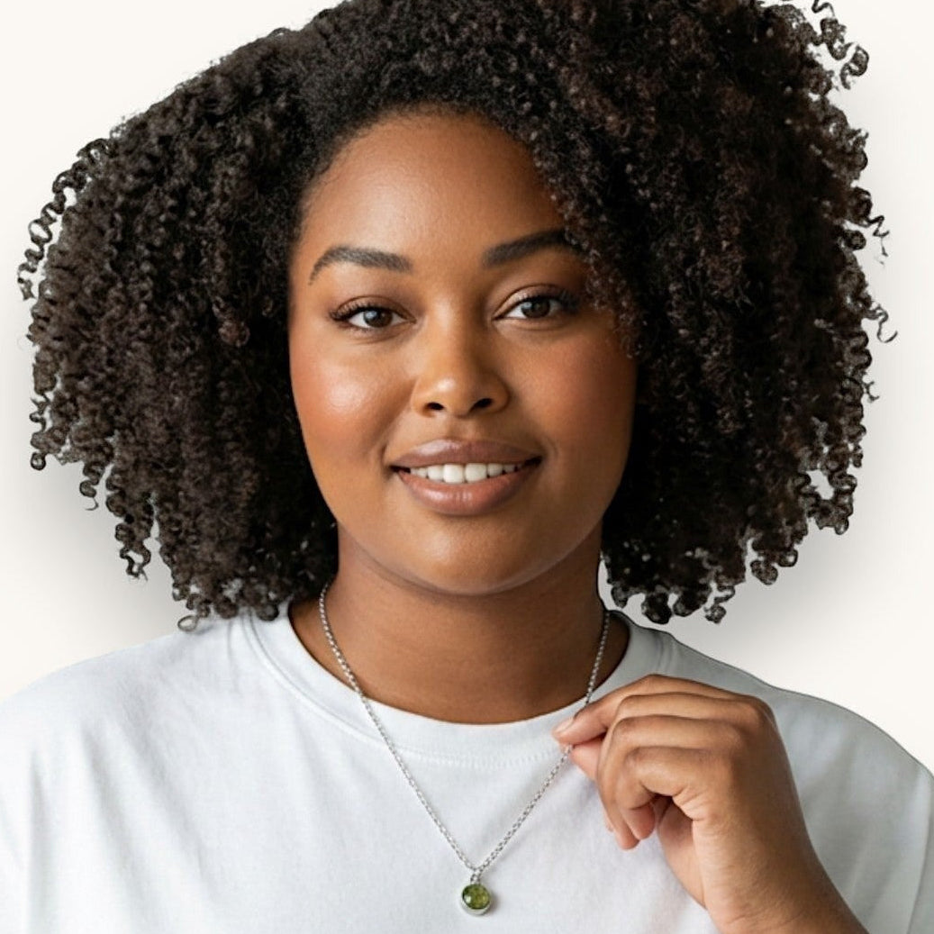 Kvinna bär ett Nayuga Jewels halsband med en rund peridotsten i silverpläterad infattning mot en vit t-shirt