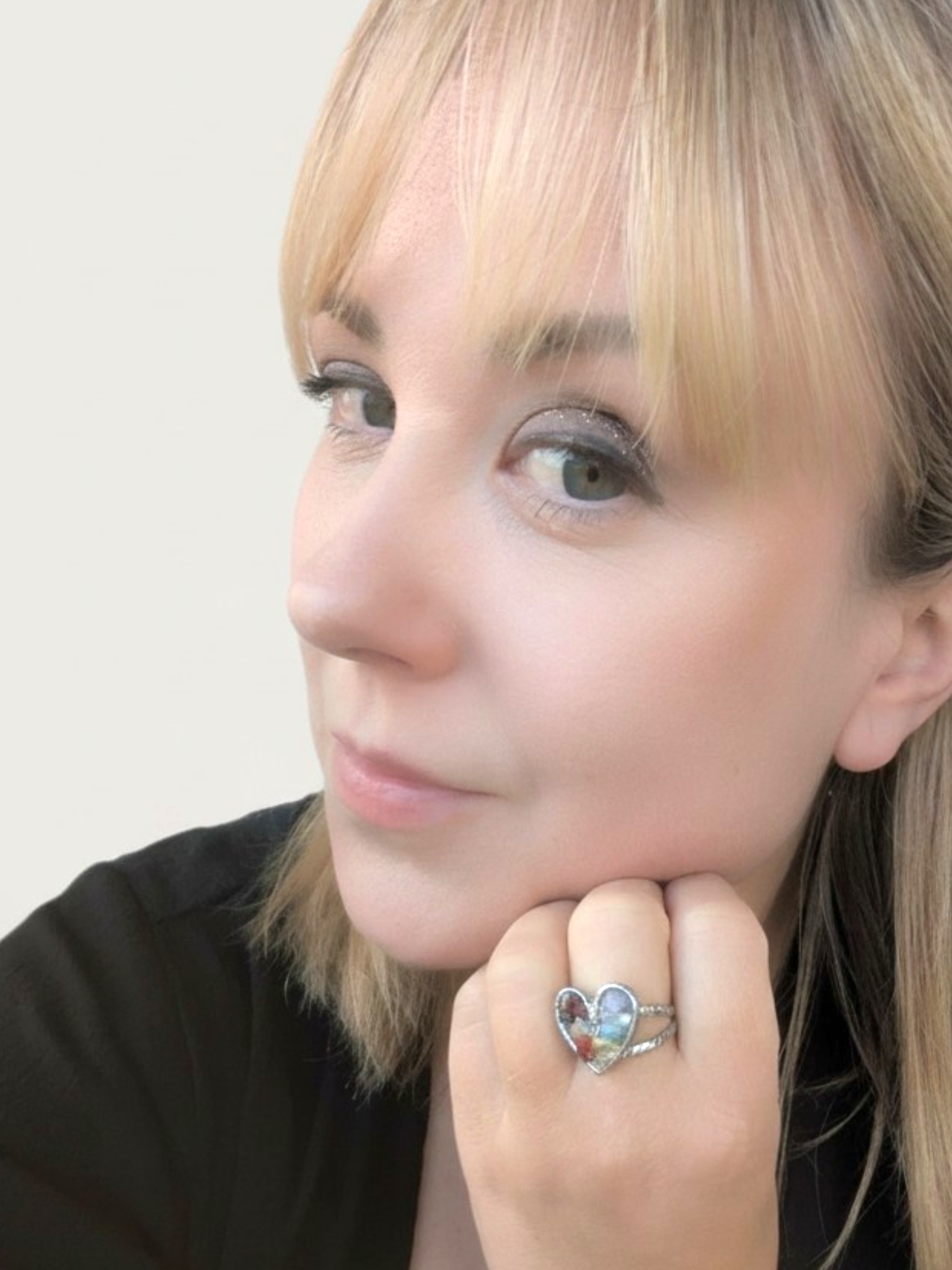 Kvinna bär Citrinmagi Pride Ring Hjärta i silver med färgglada kristaller på fingret nära ansiktet.