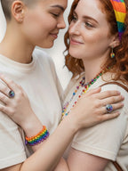 Två kvinnor bär Citrinmagi Pride Ring i silver med färgglada kristaller under en prideparad utomhus.