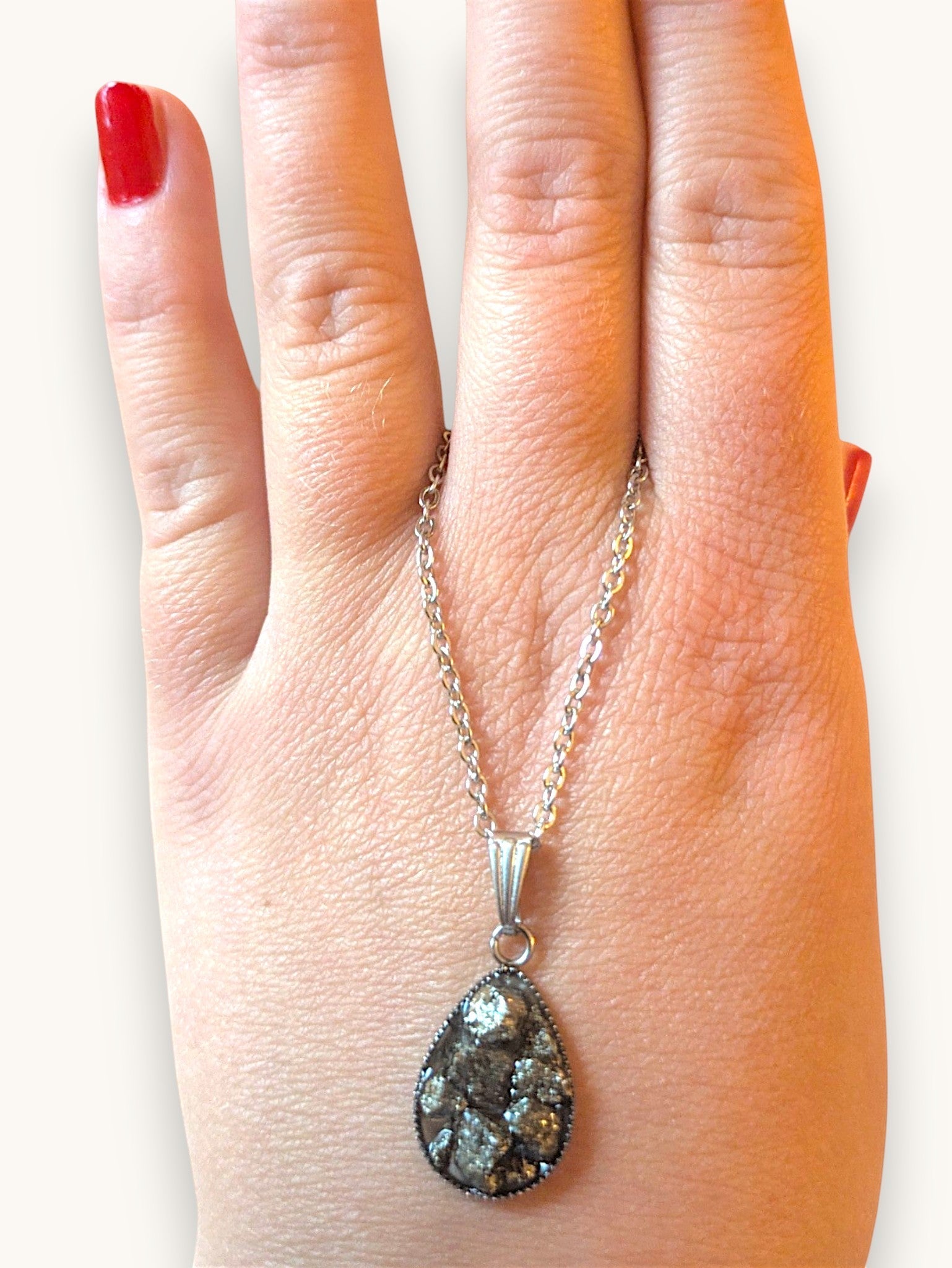 Citrinmagi halsband med droppformat hänge i silver och naturliga pyritkristaller som hålls i en hand.