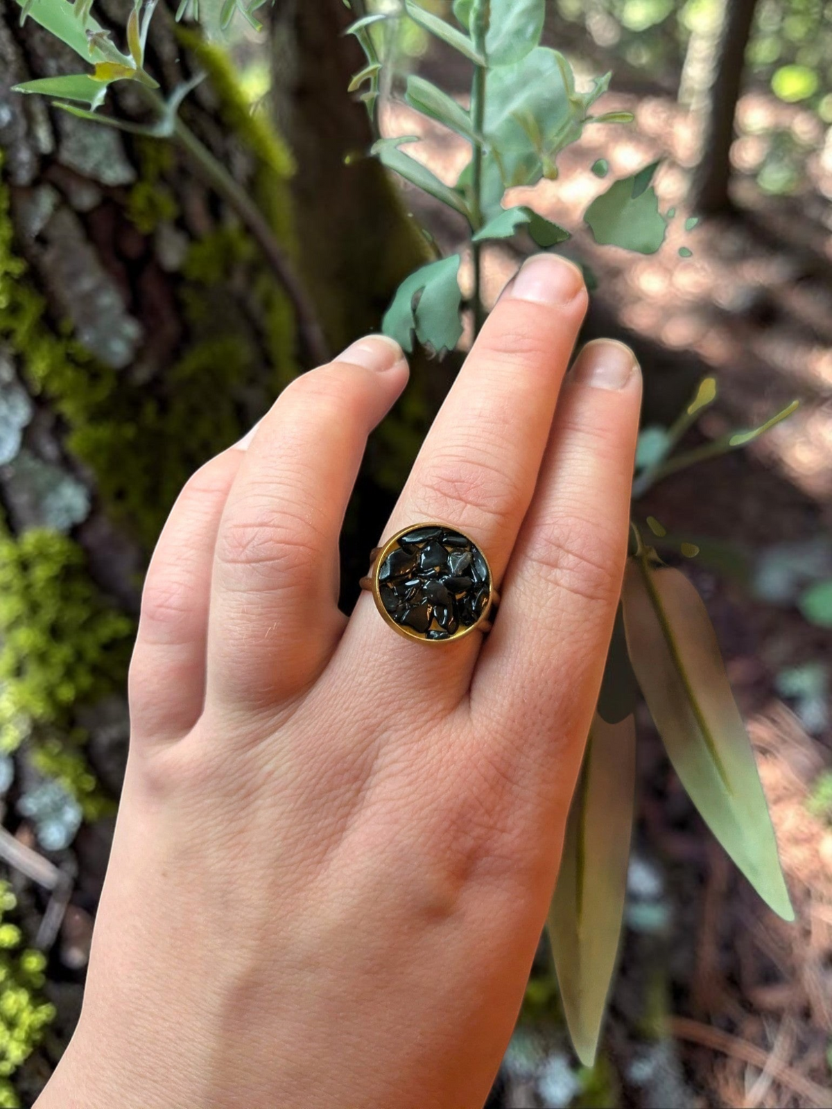 Citrinmagi rund guldring med glittrande svarta stenfragment buren på ett finger mot en bakgrund av blommor