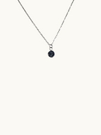 Citrinmagi silverfärgat halsband med en minimalistisk rund berlock och mörk glittrande detalj på ljus yta.